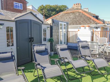 Outdoor area with grey reclining chairs on artificial grass next to a storage shed at Penmar in Looe