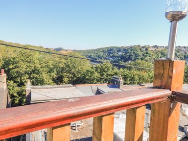 View from a wooden balcony railing over rooftops to trees and hills at Penmar in Looe