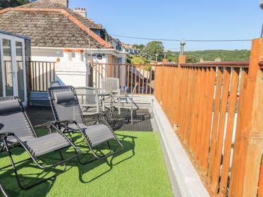 A rooftop terrace with lounge chairs a table with chairs and wooden railings at Penmar in Looe