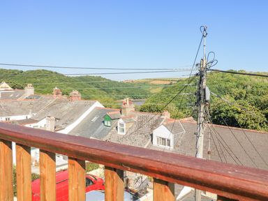 A view of rooftops with chimneys and power lines with hills in the background from behind a wooden railing at Penmar in Looe