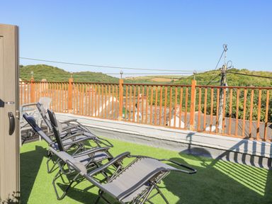 An outdoor rooftop terrace with reclining chairs and a wooden railing overlooking green hills at Penmar in Looe
