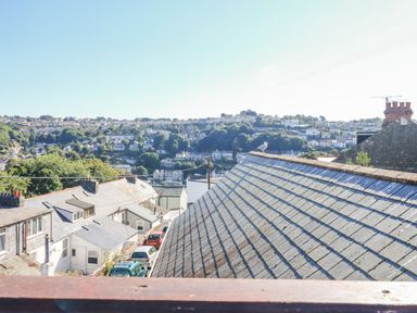 View of rooftops with houses and trees on a hillside in the background at Penmar in Looe