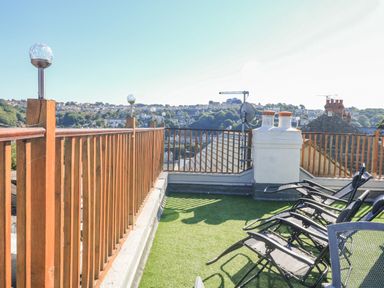 An outdoor terrace with wooden railing and black lounge chairs on artificial grass at Penmar in Looe