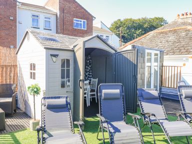 An outdoor area with reclining chairs arranged on artificial grass and small sheds with open doors at Penmar in Looe