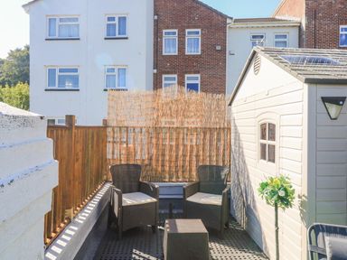 A small outdoor patio with two chairs a small table a wooden fence and a storage shed at Penmar in Looe