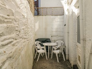A small outdoor patio area with white plastic chairs and a round table between white walls at Penmar in Looe