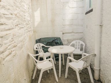A small outdoor seating area with a round white table and four white plastic chairs surrounded by white textured walls at Penmar in Looe