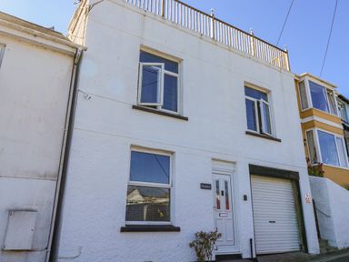 A white two-story house with windows a door and a garage door at Penmar in Looe