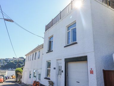 A street view of white buildings with windows and garage doors under clear sky at Penmar in Looe