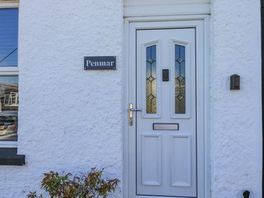 A white front door with glass panels and a mail slot next to a wall with a Penmar nameplate at Penmar in Looe