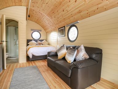 A room with a bed and a black sofa with pillows wooden floor and walls at Filbert Pod in Arundel West Sussex