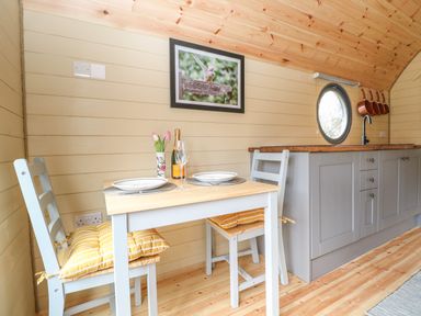 A small dining area with a table set for two and a kitchen counter with cabinets and a sink in a wooden room at Filbert Pod in Arundel West Sussex