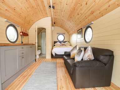An interior view of a pod with a kitchen area on the left a leather sofa with pillows on the right a bed in the back and a bathroom door open in the center at Filbert Pod in Arundel West Sussex