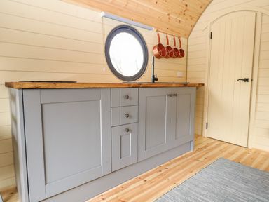 A kitchen with gray cabinets a wood countertop a round window and copper pans hanging on the wall at Filbert Pod in Arundel West Sussex