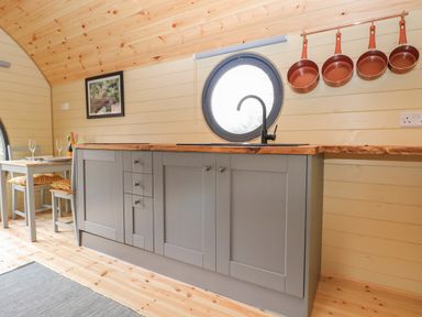 A kitchen with gray cabinets wooden countertop round window above sink and pans hanging above counter at Filbert Pod in Arundel West Sussex