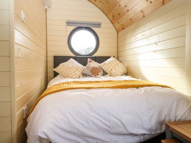 A bedroom with a double bed white bedding yellow throw pillows and a round window at Filbert Pod in Arundel West Sussex