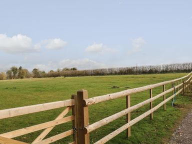 A wooden fence and gate enclosing a green grassy field with trees in the background at Filbert Pod in Arundel West Sussex
