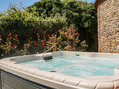 An outdoor hot tub with bubbling water near a stone wall and plants at Filbert Pod in Arundel West Sussex