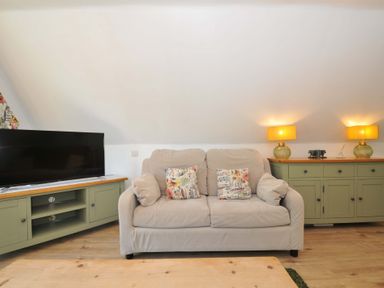 A beige sofa with floral cushions between two green wooden cabinets with lamps and a television on the left at 60 Valley Lodge in Callington near Gunnislake