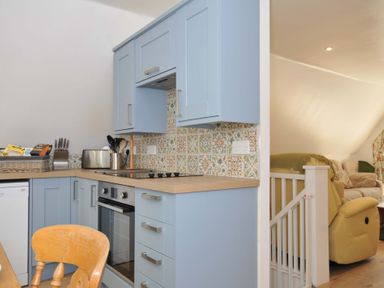 A kitchen with blue cabinets wooden countertop patterned tile backsplash and a view of a living room with beige and yellow seating at 60 Valley Lodge in Callington near Gunnislake