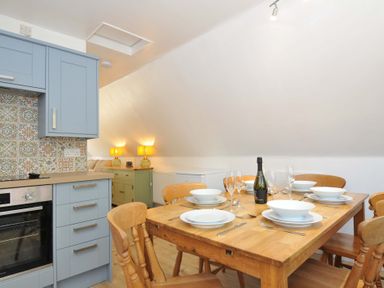 A dining table set for six with plates glasses and a bottle next to a kitchen area with blue cabinets and patterned tiles at 60 Valley Lodge Callington near Gunnislake