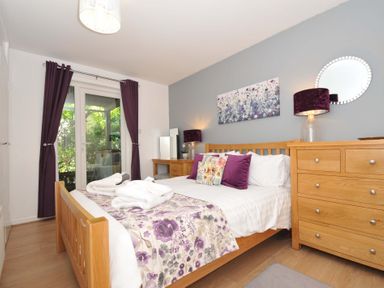 A bedroom with a wooden bed and dresser purple curtains and floral bedding at 60 Valley Lodge in Callington near Gunnislake