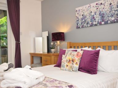 A bedroom with a wooden bed frame purple and floral cushions bedside table with lamp and mirror at 60 Valley Lodge Callington near Gunnislake