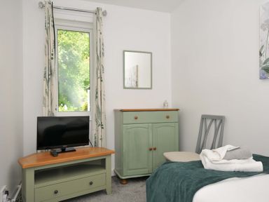 A bedroom with a television on a stand a window with curtains a cupboard a chair and a bed with towels at 60 Valley Lodge in Callington near Gunnislake