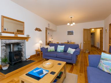 A living room with blue sofas a coffee table and a fireplace at Chynance in Porthcurno