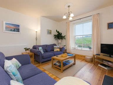 A living room with blue sofas a wooden coffee table a television and a large window at Chynance in Porthcurno