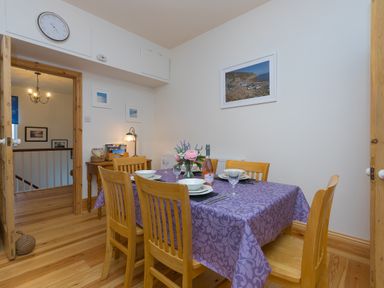 A dining room with a wooden table covered by a purple tablecloth set for four and wooden chairs at Chynance in Porthcurno