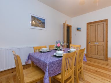 A dining room with a wooden table and chairs set with dishes and a flower vase at Chynance in Porthcurno