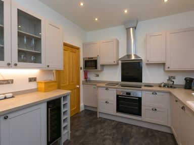 A kitchen with beige cabinets wooden countertops stainless steel oven and chimney and a wooden door at Chynance in Porthcurno