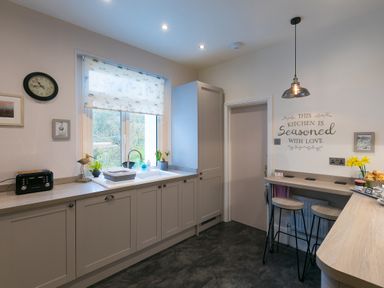 A kitchen with cabinets a window a sink a toaster and a breakfast bar with stools at Chynance in Porthcurno