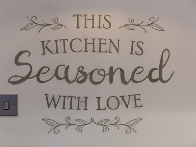 A wall with the text This kitchen is seasoned with love and decorative leaf designs
