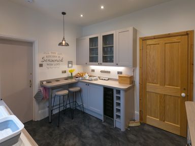 A kitchen corner with a breakfast bar stools cupboards and a wooden door at Chynance in Porthcurno