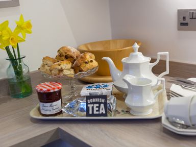 A tray with scones clotted cream jam a teapot and a milk jug with daffodils in a vase on a countertop at Chynance in Porthcurno