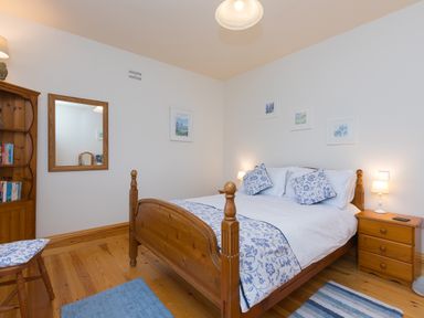 A bedroom with a wooden bed white and blue bedding wooden nightstand with lamps and wooden furniture at Chynance in Porthcurno