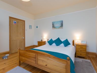 A bedroom with a wooden double bed blue cushions bedside tables lamps and wooden flooring at Chynance in Porthcurno