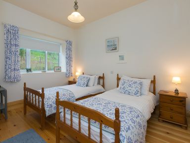 A bedroom with two single wooden beds with blue and white bedding and wooden nightstands with lamps at Chynance in Porthcurno