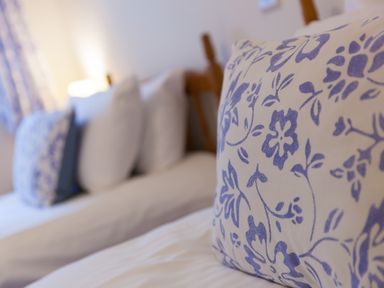 Close-up of a bed with a floral patterned pillow and white pillows in a bedroom at Chynance Porthcurno
