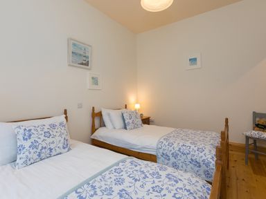 A bedroom with two single beds with blue and white floral bedding a wooden floor and wall art at Chynance in Porthcurno