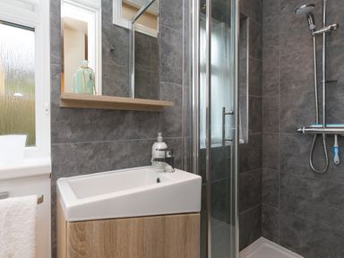 A bathroom with a sink vanity mirror shelf and a shower area with a glass door at Chynance in Porthcurno