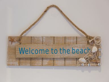 A wooden hanging sign with the text welcome to the beach decorated with shells a net and a starfish at Chynance in Porthcurno