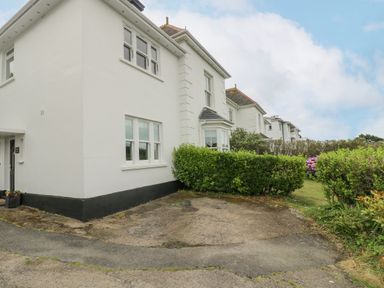 A white two story house with black trim and green hedges in front at Chynance in Porthcurno