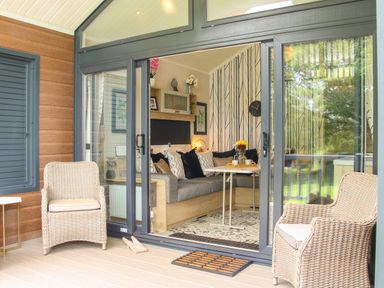 A seating area with wicker chairs outside sliding glass doors leading to a living room with a corner sofa and a table at Jacob's Meadow Pod 2 in Minsterley near Chirbury