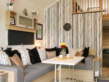 A living room with a corner sofa a table and a clock on the patterned wall at Jacobs Meadow Pod 2 in Minsterley near Chirbury