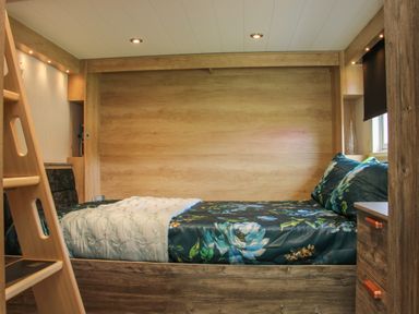 A bedroom with a bed featuring floral bedding and a wooden ladder and drawers at Jacobs Meadow Pod 2 in Minsterley near Chirbury