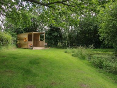 A wooden shelter with two benches and a life ring beside a pond surrounded by trees at Jacobs Meadow Pod 2 in Minsterley near Chirbury