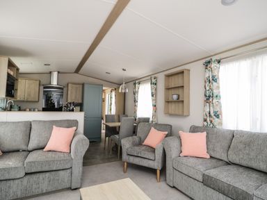 A living room with grey sofas and pink cushions next to a dining area with a wooden table and grey chairs at Burlees Nest in Brigham near Great Broughton Cockermouth